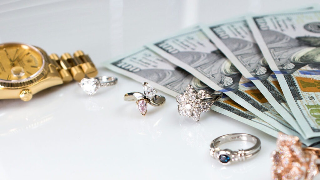 close up of diamond rings, gold watch, and 100 dollar bills