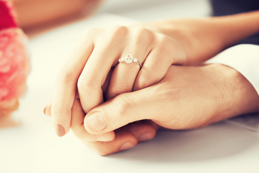 man and woman holding hand with engagement ring